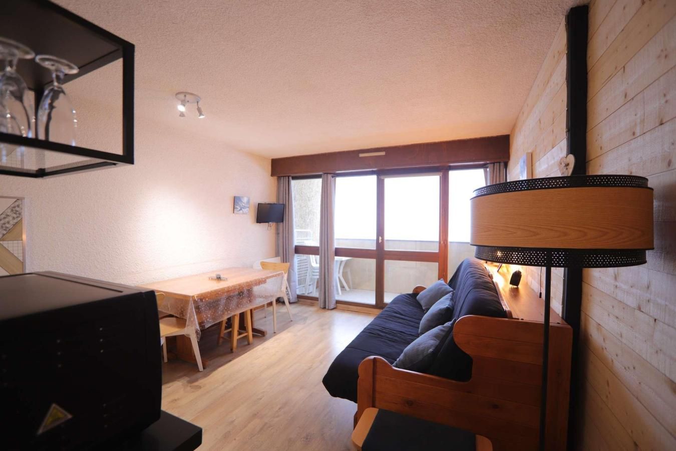 A room with a wooden floor, a sofa, a table, a TV, and a large window.