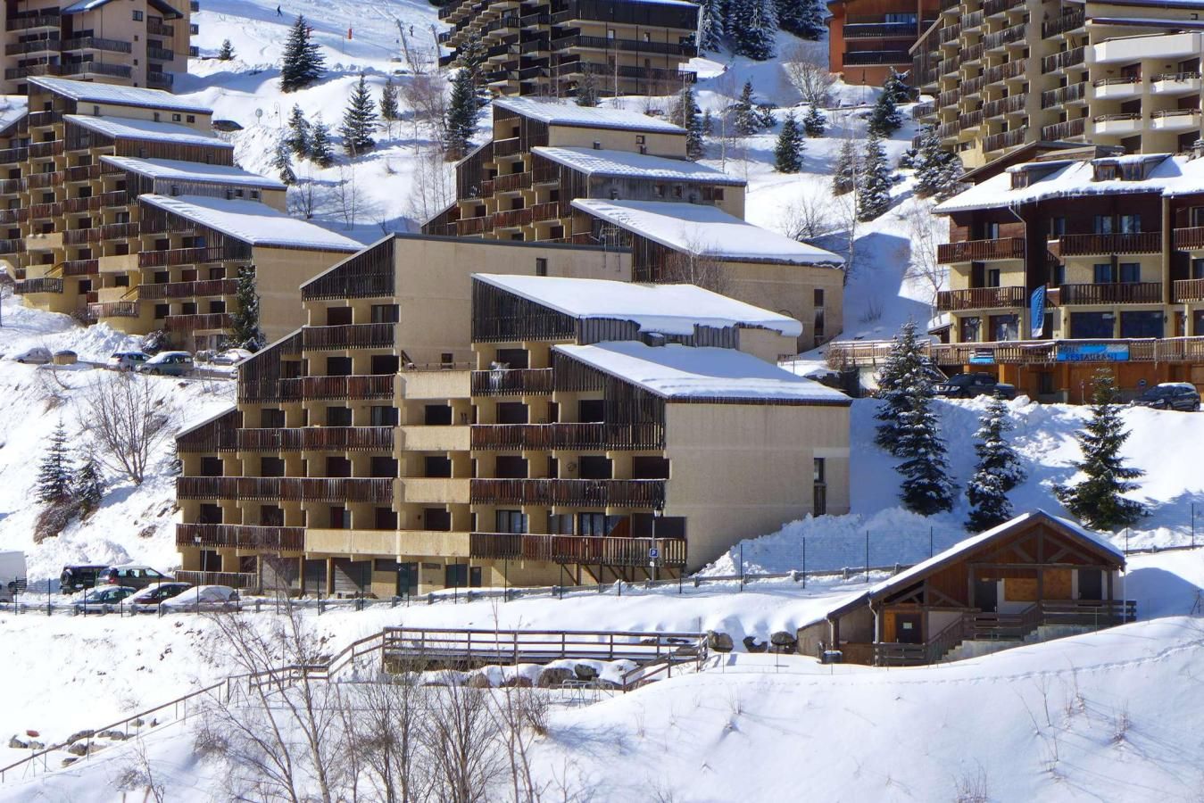 Ein schneebedecktes Resort mit mehrstöckigen Gebäuden, Balkonen und einer Skipiste im Hintergrund.