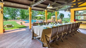 A covered outdoor dining area with a pool and garden view.