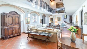 A spacious living room with a high ceiling, a wooden cabinet, a sofa, and a dining table with a vase of flowers.