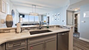 Une cuisine moderne dotée d’un grand îlot central, d’appareils électroménagers en acier inoxydable et offrant une vue sur l’extérieur.