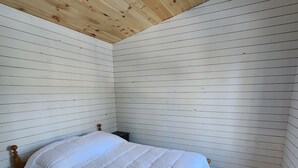 Une pièce avec un lit en bois, des murs blancs et un plancher en bois.