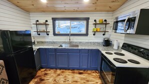 Une cuisine avec un plancher en bois, des armoires bleues, un réfrigérateur noir, une cuisinière et un four à micro-ondes.