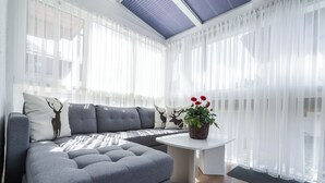 Ein modernes Wohnzimmer mit einem grauen Ecksofa, einem kleinen weißen Tisch und transparenten Vorhängen.