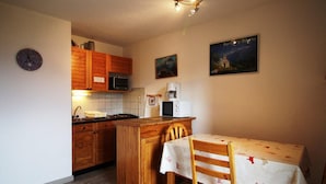 Una cocina compacta con armarios de madera, un microondas, una cafetera y una mesa de comedor con mantel.