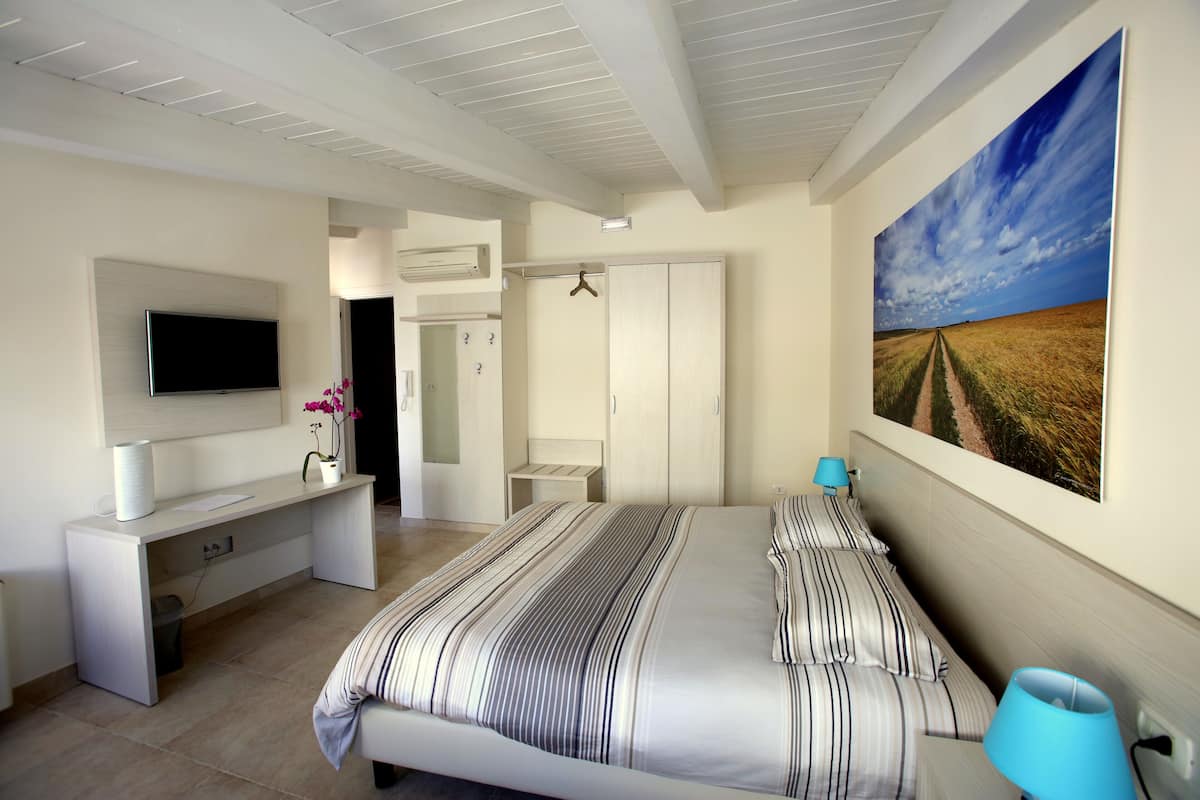A bedroom with a bed, a TV, a desk, a wardrobe, and a painting on the wall.