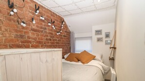 Un dormitorio con pared de ladrillo, estructura de cama de madera, techo blanco y una ventana con persianas.