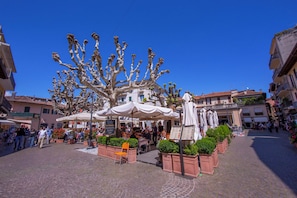 A cobblestone square with outdoor seating, a fountain, and surrounding buildings.
