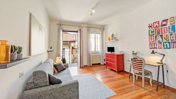 A modern living room with a sofa, a desk, and a chair. There is a view of the outside through a door. - Casa Rachele Stresa Center (Stresa)