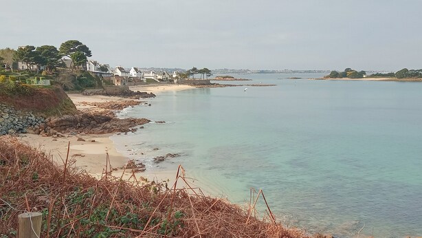 Une vue sur la côte, avec une plage de sable, une eau claire et des maisons qui bordent le rivage.