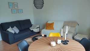 Un salon moderne avec un canapé foncé, une table ronde en bois entourée de chaises et un fauteuil jaune.