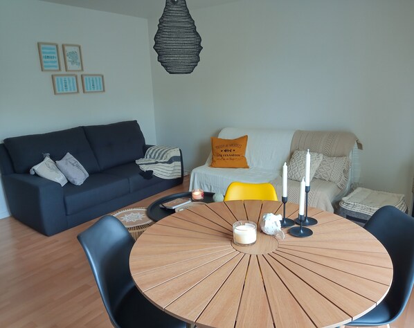 Una sala de estar moderna con un sofá oscuro, una mesa redonda de madera y sillas, y una butaca amarilla.