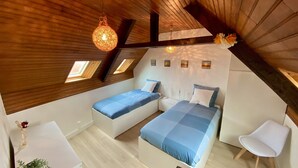 Un dormitorio abrigado en el ático con dos camas, una pequeña silla blanca y una lámpara colgante.