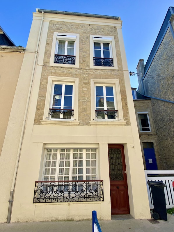 Un immeuble à plusieurs étages, doté d’une façade beige, de fenêtres à encadrement blanc et de balcons ornés de garde-corps en fer forgé.