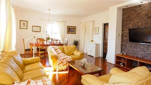 Una sala de estar con sofás amarillos, una mesa de comedor y un televisor montado en una pared de piedra.