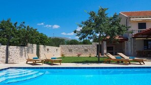 Una piscina con sillas de descanso, un muro de piedra y un edificio con tejado de baldosas.