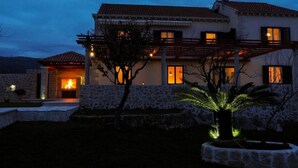 Una casa de dos pisos con fachada de piedra, una chimenea visible y una entrada bien iluminada.