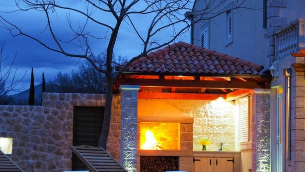 Cocina al aire libre con paredes de piedra, una chimenea, sillones de madera y un farol.