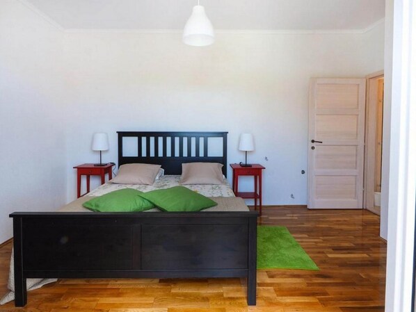 A bedroom with a wooden bed, two bedside tables with lamps, a green rug, and a white door.