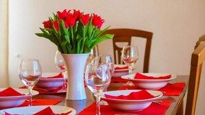 Una mesa de comedor dispuesta con servilletas rojas, platos blancos y copas de cristal para vino, junto a un jarrón con tulipanes rojos.