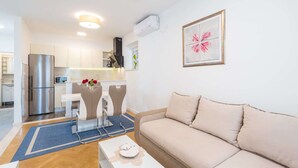 A modern living room with a beige sofa, a white coffee table, and a dining area with a white table and chairs. - Apartments Lucija - Two Bedroom Apartment With Balcony and Sea View (Dubrovnik)