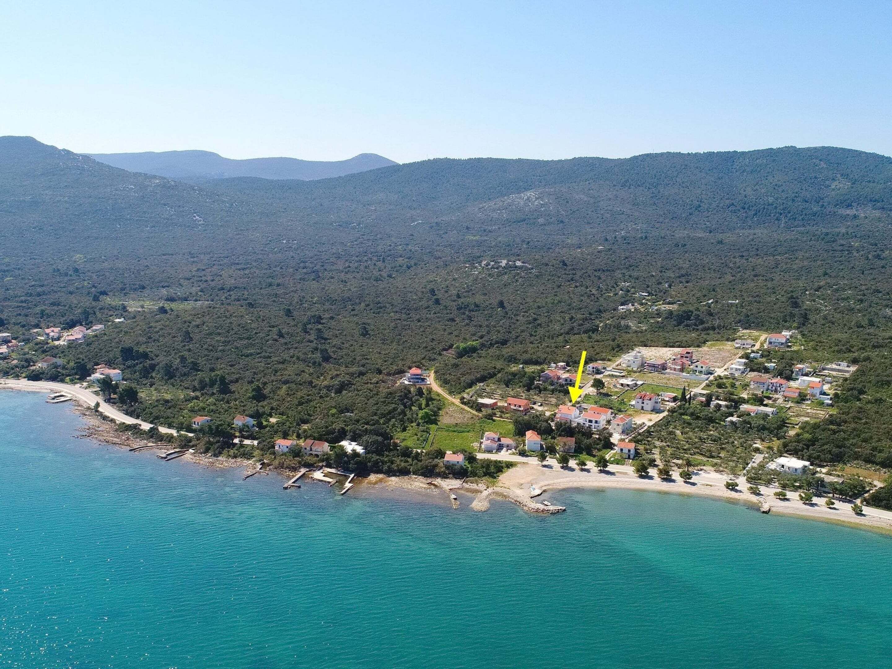 An aerial view of a coastal town with a beach, houses, and a forested area.