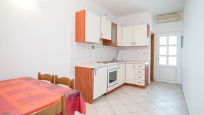 A compact kitchen with white cabinets, a stove, and a sink. There is a dining table with chairs. - Apartments Neva- One Bedroom Apartment (Selca)