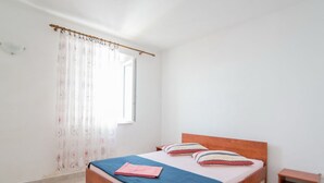A bedroom with a wooden bed, a blue blanket, and two pillows. - Apartments Neva- One Bedroom Apartment (Selca)