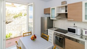 A compact kitchen with a refrigerator, microwave, and stove. There's a dining table with chairs and a vase of flowers. - Apartments Bonavista - Premium Two Bedroom Apartment With Balcony and Sea View (Dubrovnik)