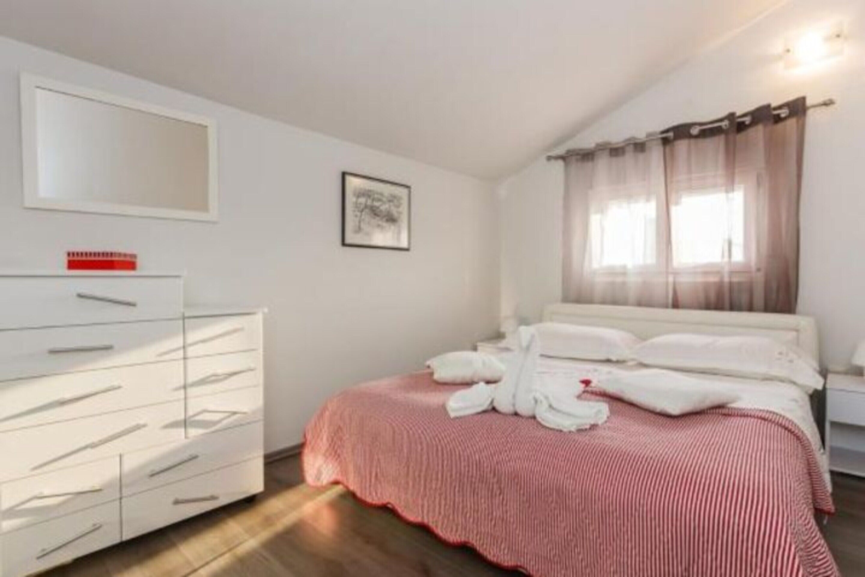 A bedroom with a bed, white dresser, and a window with sheer curtains.