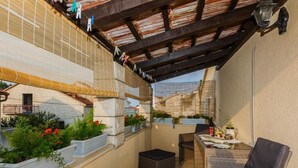 A covered outdoor seating area with wicker furniture, potted plants, and a table with a bottle and glasses. - Apartments Roda - Comfort One Bedroom Apartment With Terrace - (Supetar)