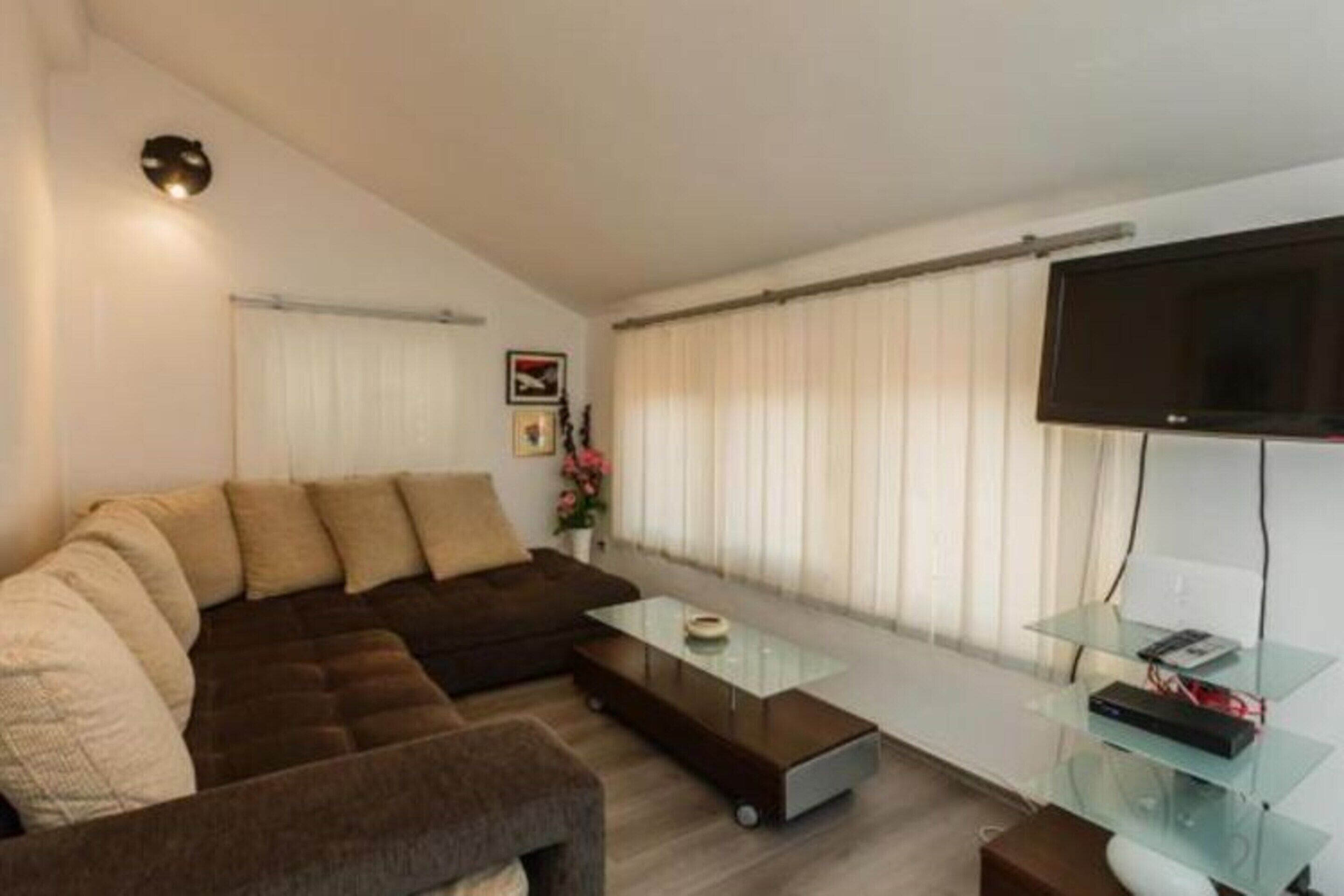 Un salon moderne avec un canapé d’angle, une table basse en verre et un téléviseur à écran plat fixé au mur.