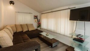 A modern living room with a sectional sofa, a glass coffee table, and a flat-screen TV mounted on the wall. - Apartments Roda - Comfort One Bedroom Apartment With Terrace - (Supetar)