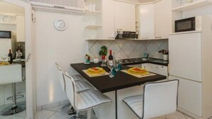 A compact kitchen with white cabinets, a black countertop, and a dining area with two chairs. - Apartments Roda - Comfort One Bedroom Apartment With Terrace - (Supetar)