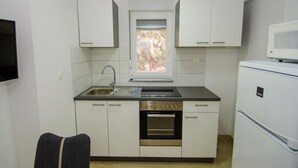 Eine kompakte Küche mit weißen Schränken, einem eingebauten Backofen, einer Mikrowelle und einem Fenster über der Spüle.