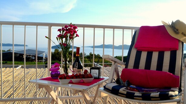 A balcony with a table set for a meal, a chair with a striped cushion, and a bottle of wine. - Apartments Lina - Three Bedroom Apartment With Two Balconies and Sea View (Dubrovnik)