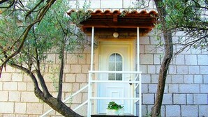 A stone building with a small balcony attached to a window, surrounded by trees. - Apartments Lina - Three Bedroom Apartment With Two Balconies and Sea View (Dubrovnik)