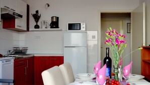 A compact kitchen with a dining area. It includes a microwave, a coffee maker, and a refrigerator. The dining table is set with plates, glasses, and a vase with flowers. - Apartments Lina - Three Bedroom Apartment With Two Balconies and Sea View (Dubrovnik)