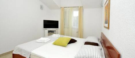 A neatly made bed with a checkered bedspread, a green pillow, and two patterned pillows. There is a television on a small white stand to the left of the bed.