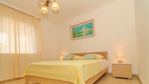A neatly arranged bedroom with a bed, bedside lamps, a nightstand, a painting on the wall, and a window with curtains. - Apartments Villa Marijana - One Bedroom Apartment With Terrace and Garden View (Blato)