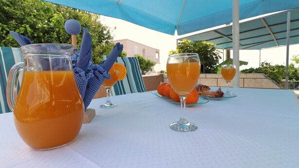 A table set outdoors with a pitcher of orange juice, two wine glasses, and a plate with pastries. - Apartments Villa Marijana - One Bedroom Apartment With Terrace and Garden View (Blato)