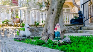 A garden with a swan statue, a tree, and a statue of a man holding a red apple. - Villa Kosa - Two Bedroom Apartment With Terrace and Sea View (Brela)