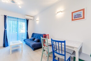 A modern living room with a blue sofa, a white table, and a blue and red chair. - Apartment Karlo - Two Bedroom Apartment With Balcony (Kastela)