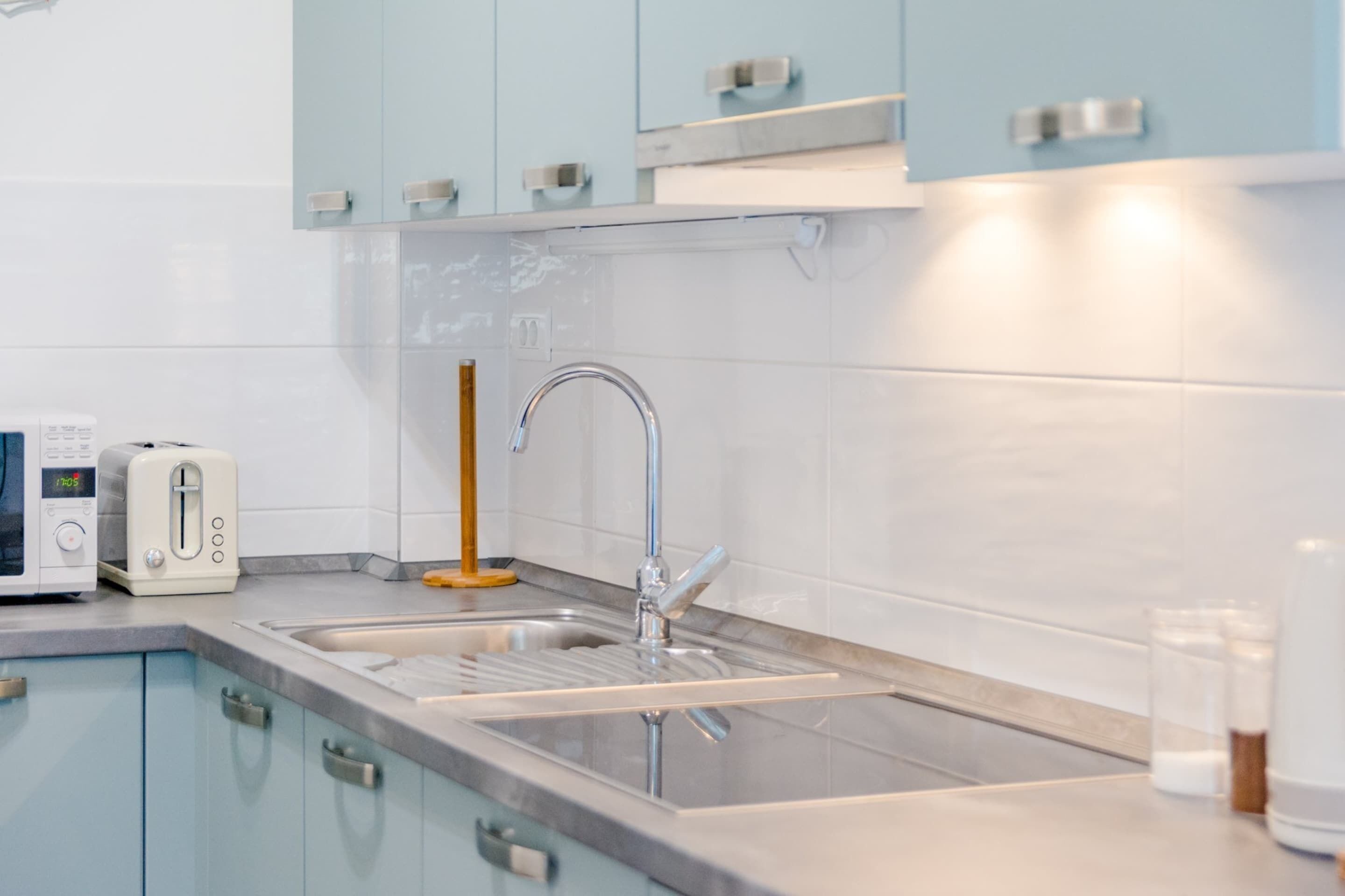 Una cocina moderna con armarios azul claro, un lavamanos de acero inoxidable, un tostador y una cuchara de madera sobre la encimera.