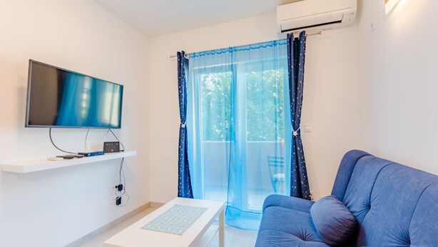 Un salon moderne doté d’un téléviseur à écran plat, d’un canapé, d’une table basse et d’un balcon agrémenté de rideaux bleus.
