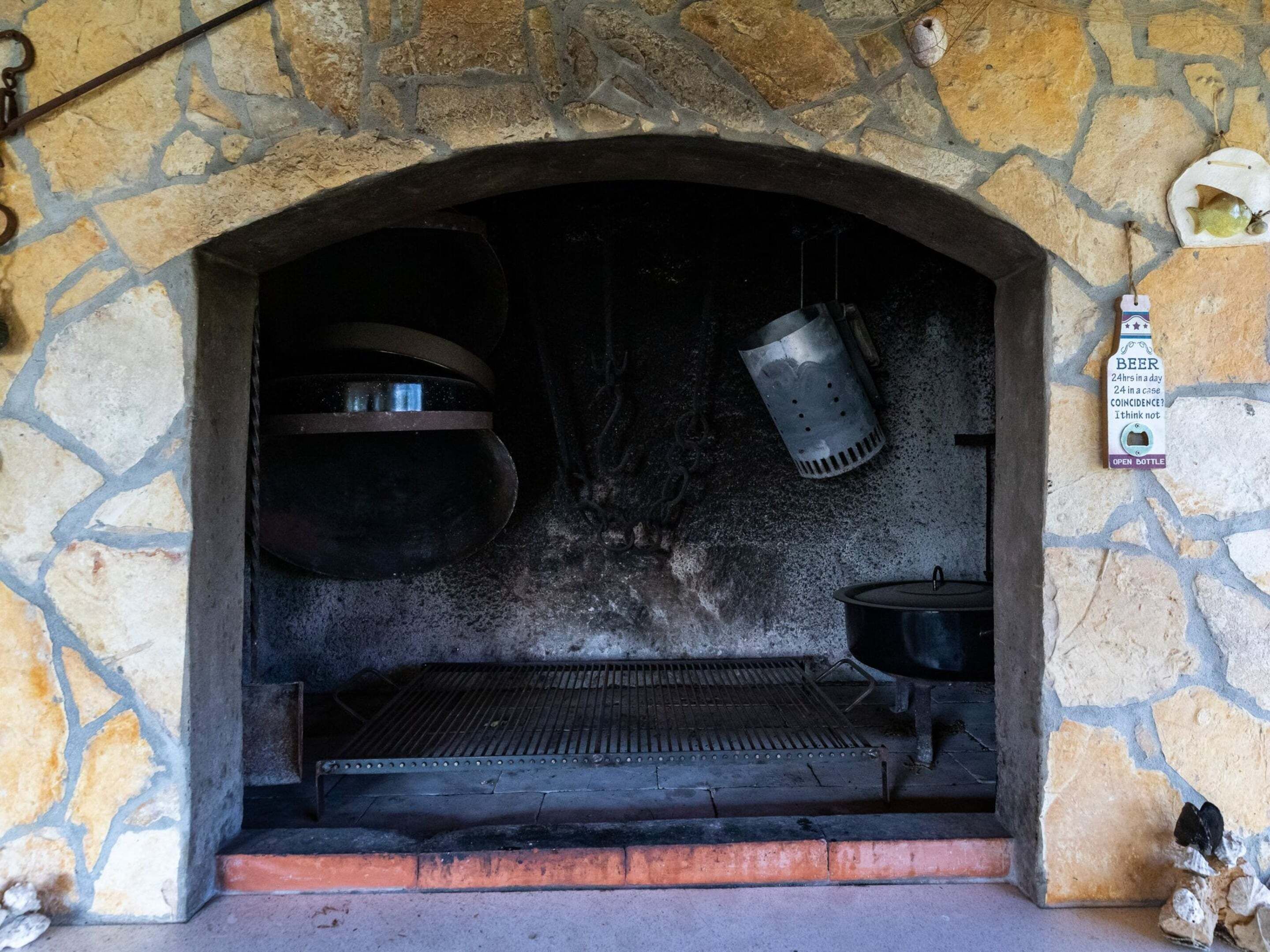 A stone archway leading to a brick oven with a metal grate and hanging cooking utensils.