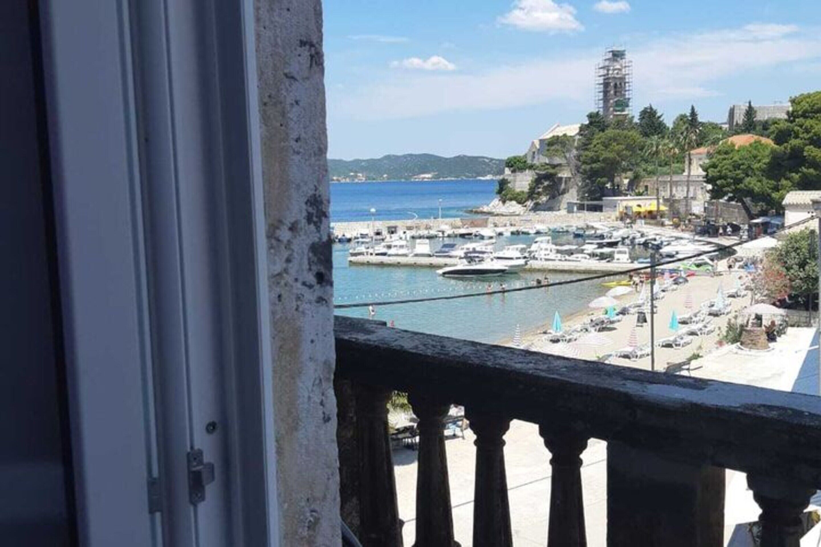 A coastal view from a balcony overlooking a marina with boats, a clear sky, and a building with scaffolding.