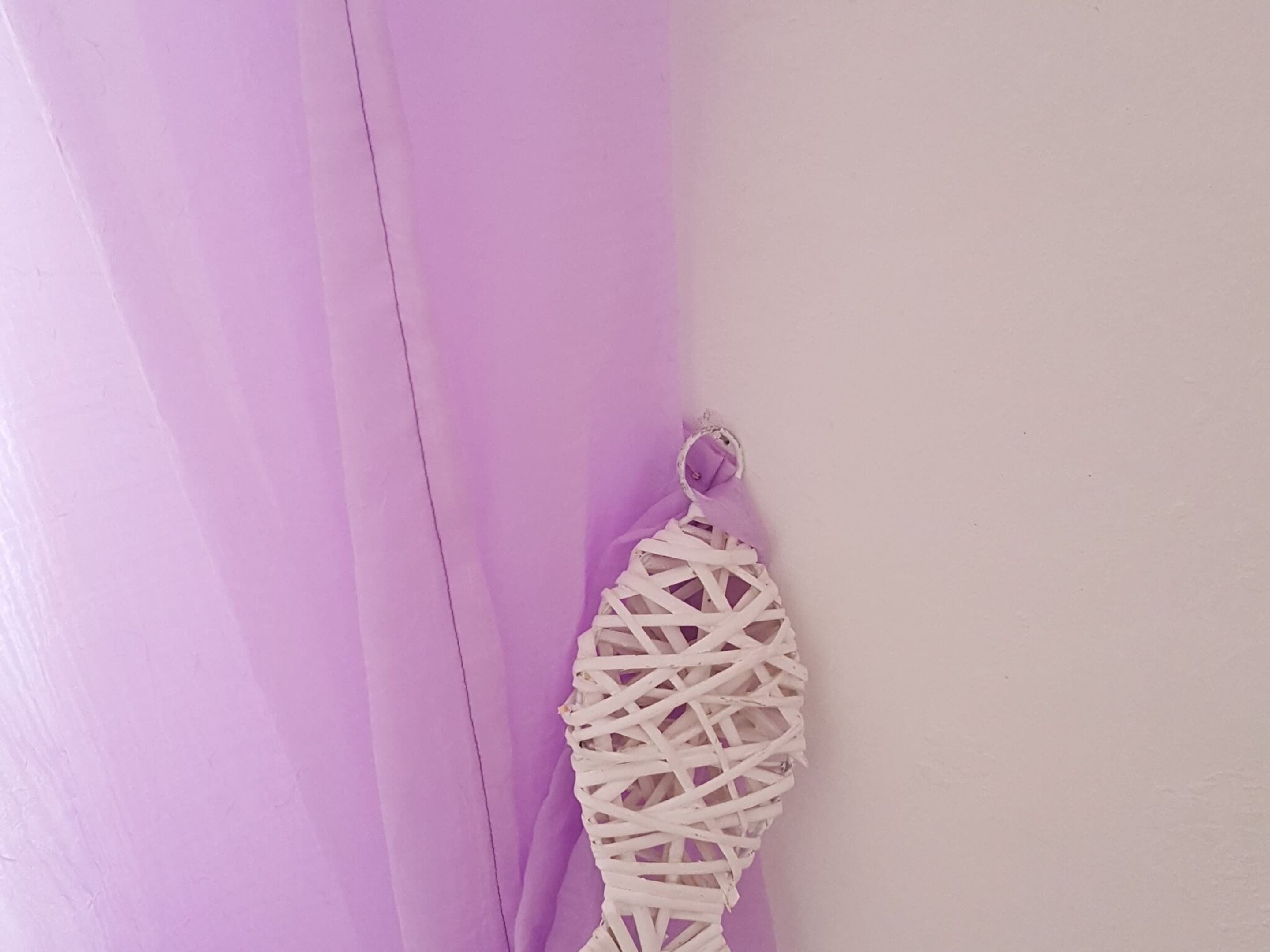 Un rideau violet orné d’une décoration murale tissée blanche.