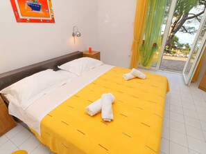 A hotel room with a bed, a nightstand, a wall-mounted lamp, and a view of the outdoors. - Apartments More & Ja - One Bedroom Apartment With Terrace and Sea View (Ston)