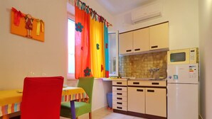 A small kitchen with a refrigerator, microwave, and cabinets. There is a dining table with chairs and a window with curtains. - Apartments More & Ja - One Bedroom Apartment With Terrace and Sea View (Ston)